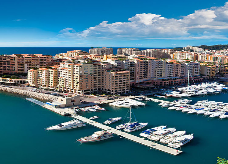 Lines of boats docked at piers on Monaco's coastline.