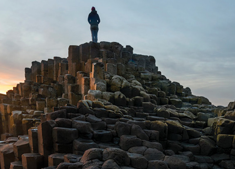 Topdeck traveler standing atop Giant's Causeway in Ireland during sunset.