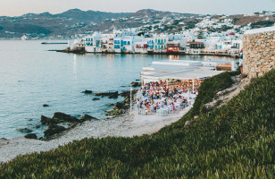 A view of the coast of Mykonos, with a beachside restaurant in the foreground.