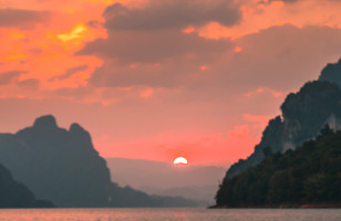 Topdeck tourist standing over the edge of a pier looking out over Thailand's famous Khao Sok National Park during sunset.