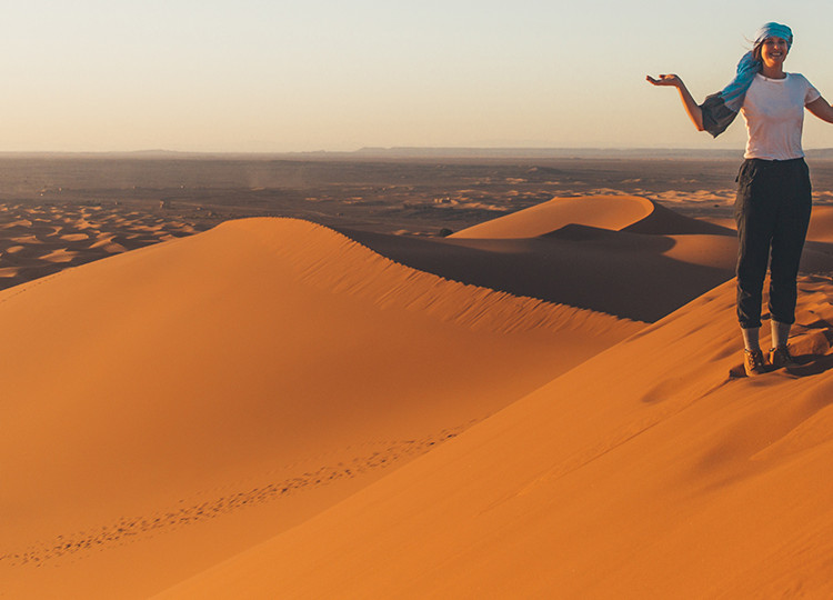 Topdeck Traveler standing alone atop a sand dune in the Sahara Desert during sunset.