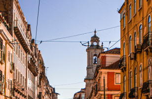 Colorful buildings surround enclose the street on a sunny afternoon in Lisbon.