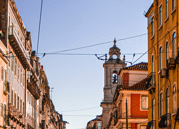 Colorful buildings surround enclose the street on a sunny afternoon in Lisbon.