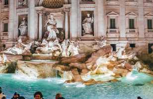 The famous Trevi Fountain of Rome lit up at night with a crowd of people surrounding it.