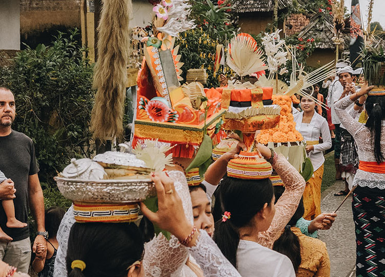 Bali people holding fruit on top of their heads parading down a road celebrating the day of silence.