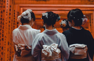 Three ladies in a kimono walking under Torii gates at the Fushimi Inari Shrine